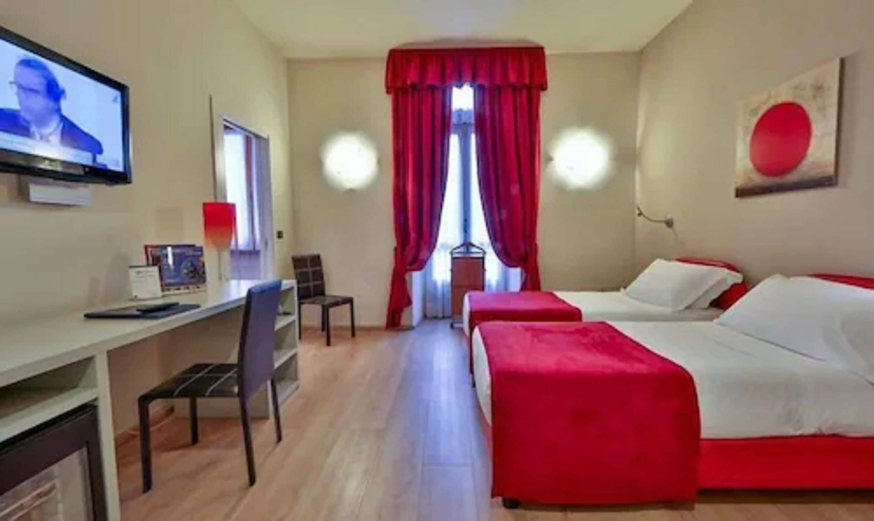 A hotel room with two beds, a desk, and a TV.