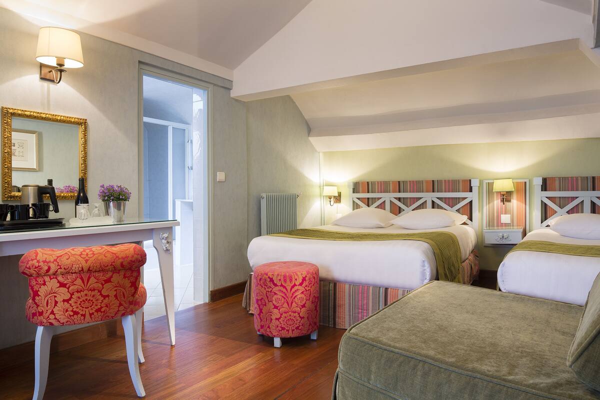 Una camera d'albergo con due letti, una scrivania con uno specchio e una sedia.