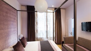 A modern hotel room with a large bed, a sofa, a television mounted on the wall, and a large window with curtains. - Hôtel Louvre Bons Enfants (Paris)