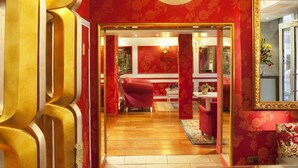 A room with red floral wallpaper, a red chair, and a mirror with a gold frame. - Hôtel Louvre Bons Enfants (Paris)