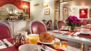 A breakfast setting with a table set for two, including croissants, orange juice, and a vase of flowers. - Hôtel Louvre Bons Enfants (Paris)