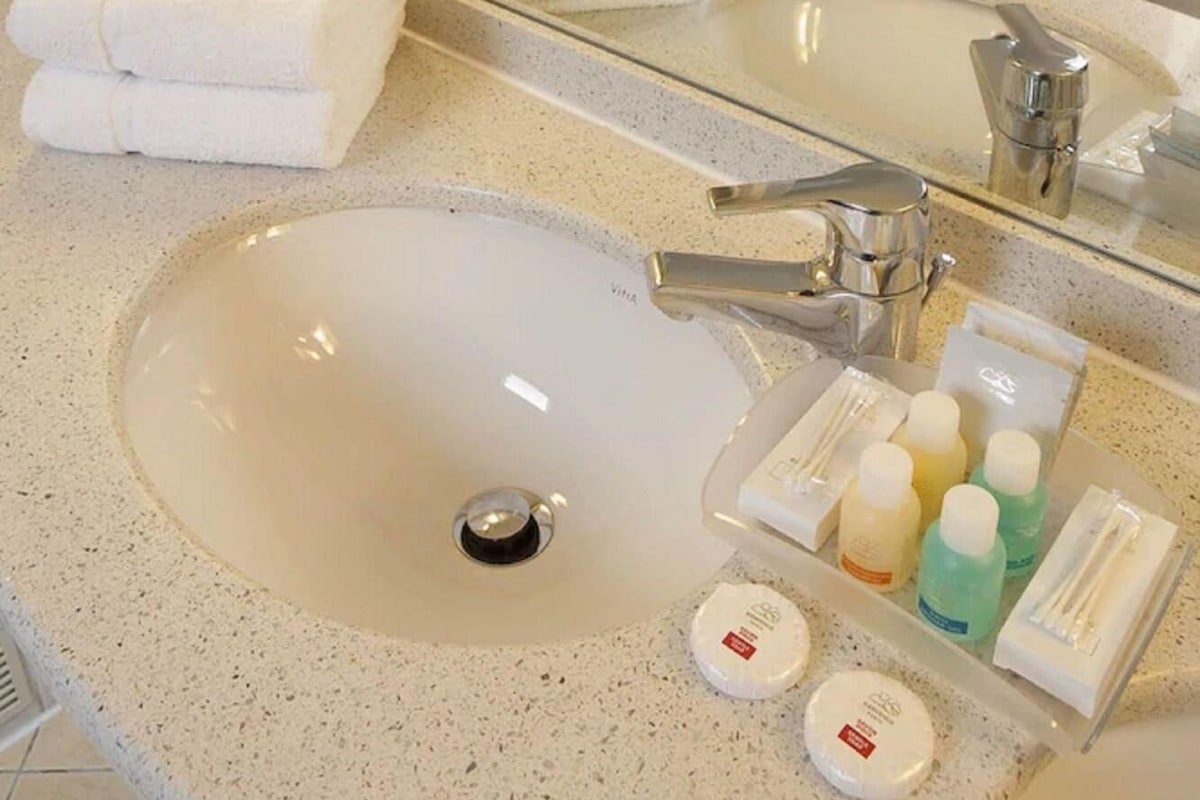 A bathroom with a large sink, a mirror, and a toilet. There are towels stacked on the counter and toiletries on the sink.