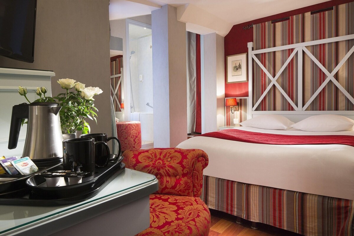 A hotel room with a bed, a bedside table with a tray of breakfast items, a red upholstered chair, and a striped wall.