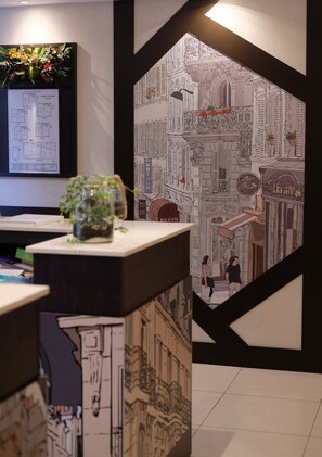 A reception area with a black and white patterned wall, a reception desk with a plant, and a monitor displaying a hotel layout. - Hotel Amiral Fondary (Paris)