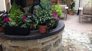 A stone planter with various potted plants and a wooden structure with a sloped roof. - Hotel Amiral Fondary (Paris)