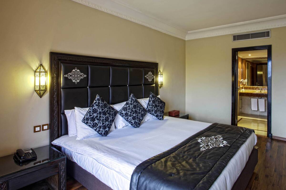 A neatly made bed with a tufted headboard, two bedside lamps, and a nightstand with a telephone.
