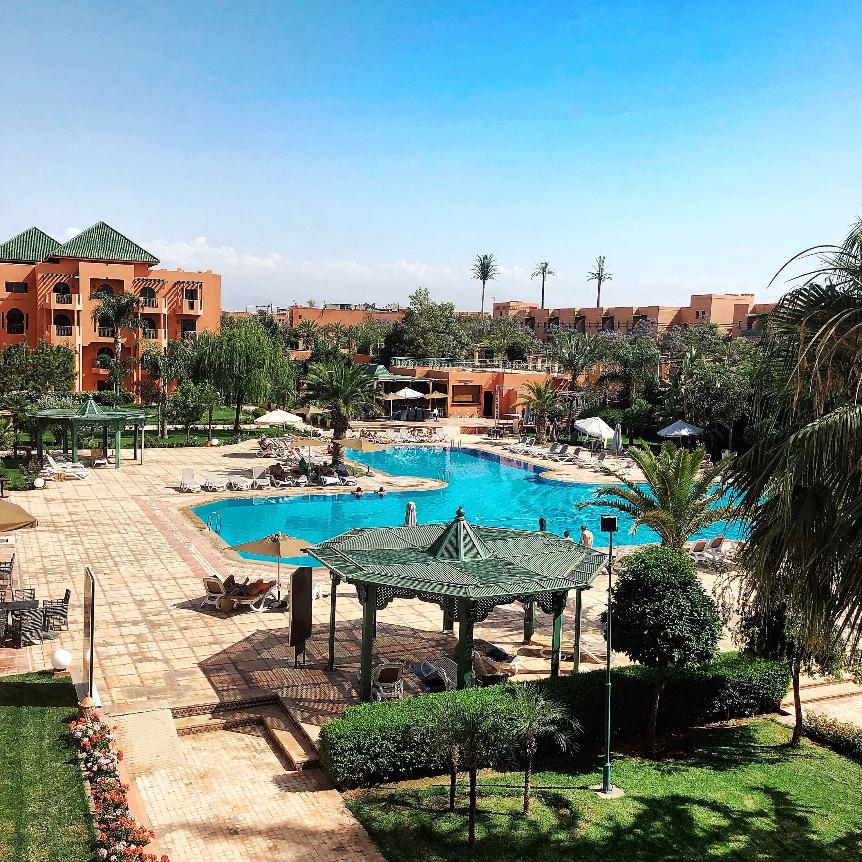 A resort with a large swimming pool, sun loungers, and a gazebo.