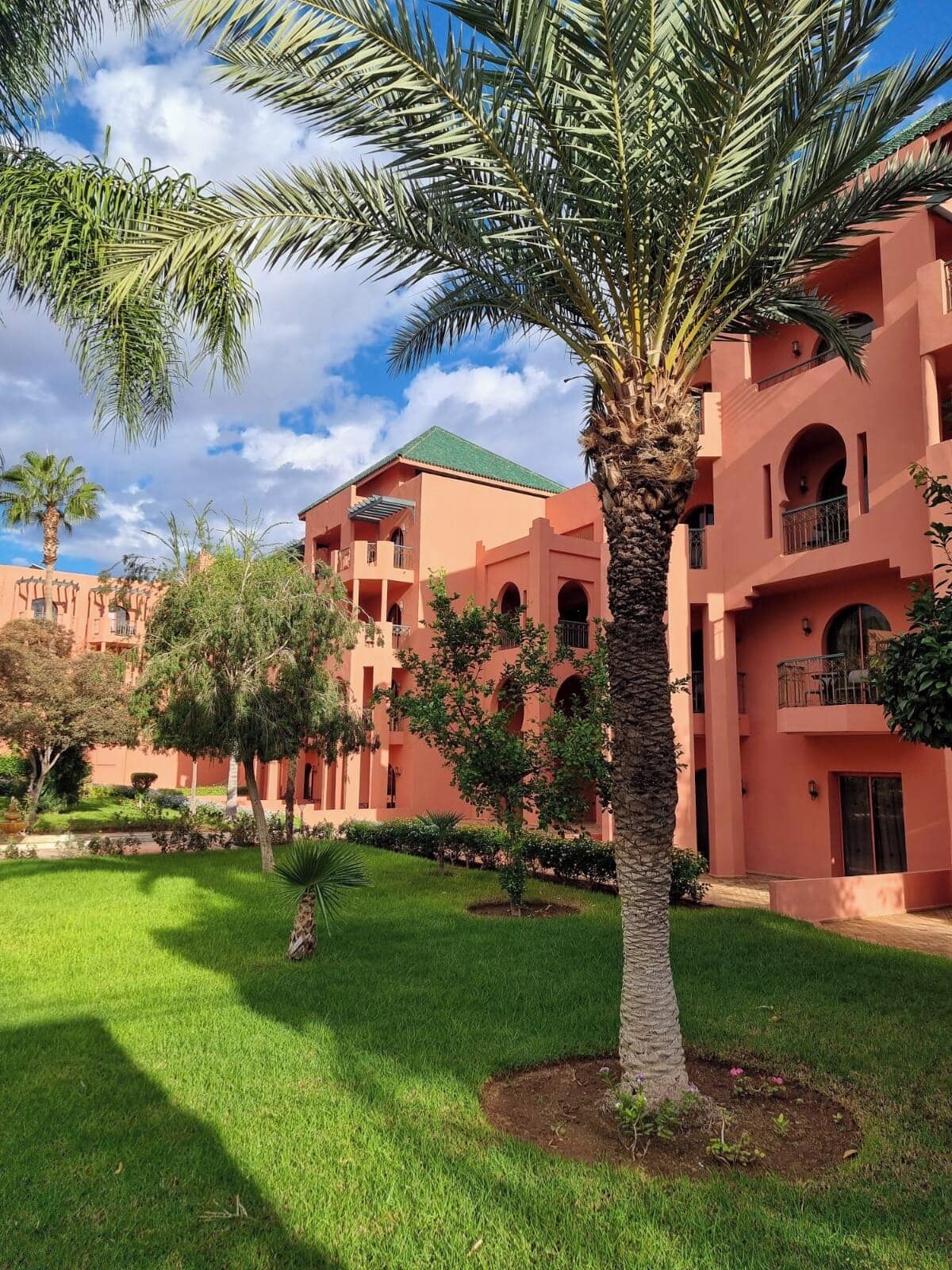 A building with multiple balconies and a well-maintained garden with palm trees.