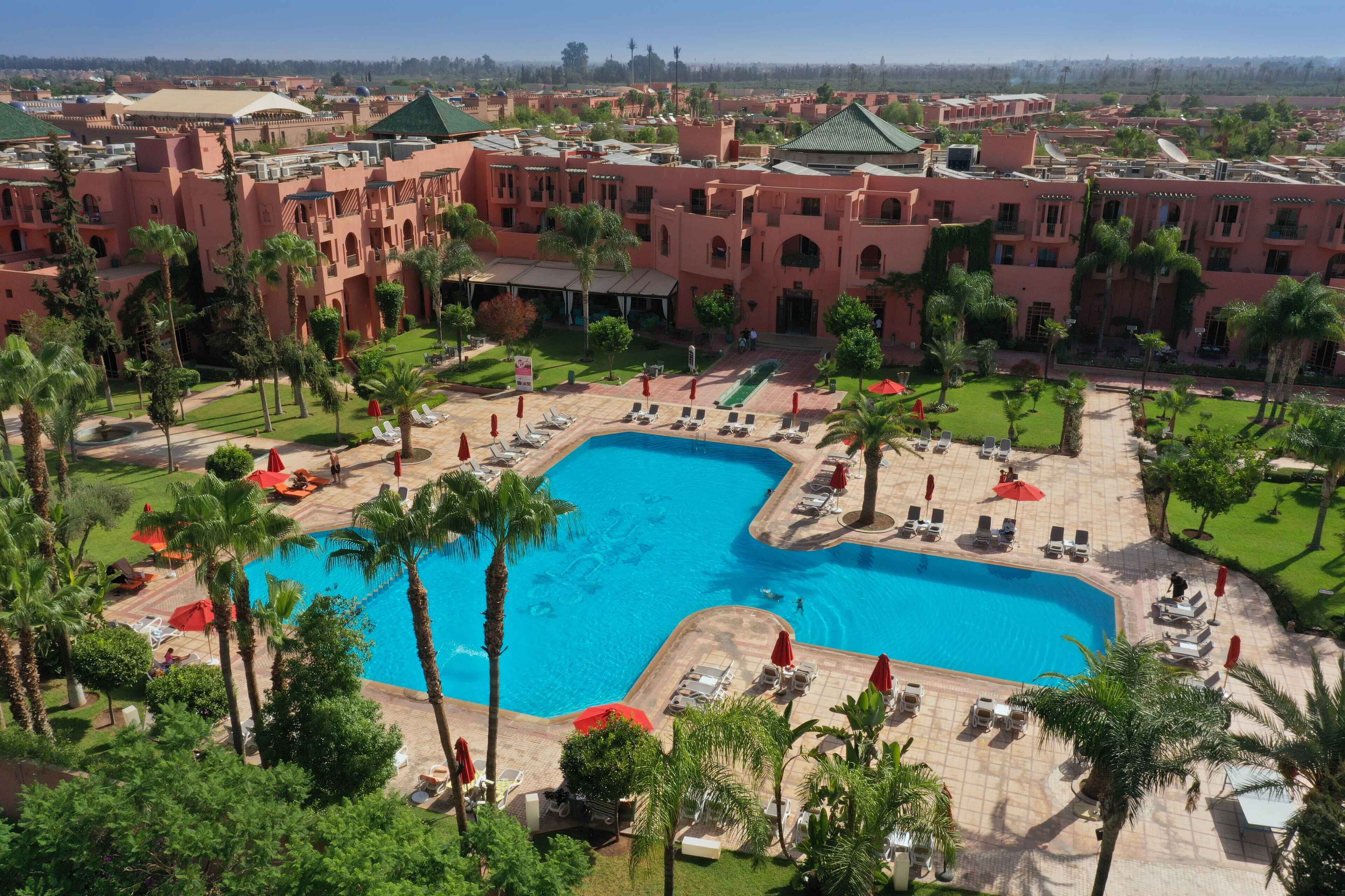 A resort with a large swimming pool surrounded by palm trees and sun loungers.