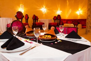 Una mesa de comedor dispuesta con servilletas negras, copas de vino y una tagine marroquí tradicional.