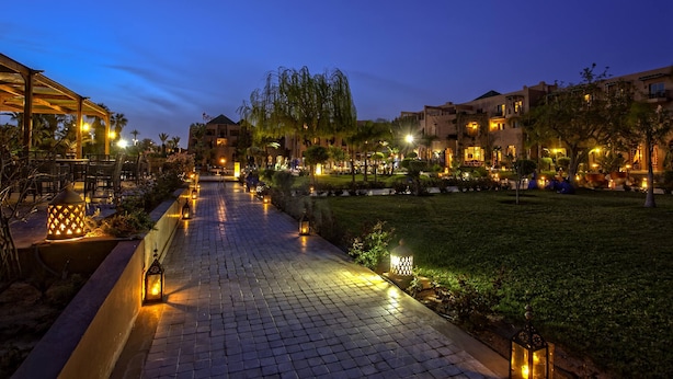 Un sendero pavimentado bordeado de faroles que conduce a un edificio con varios balcones y un jardín bien iluminado.