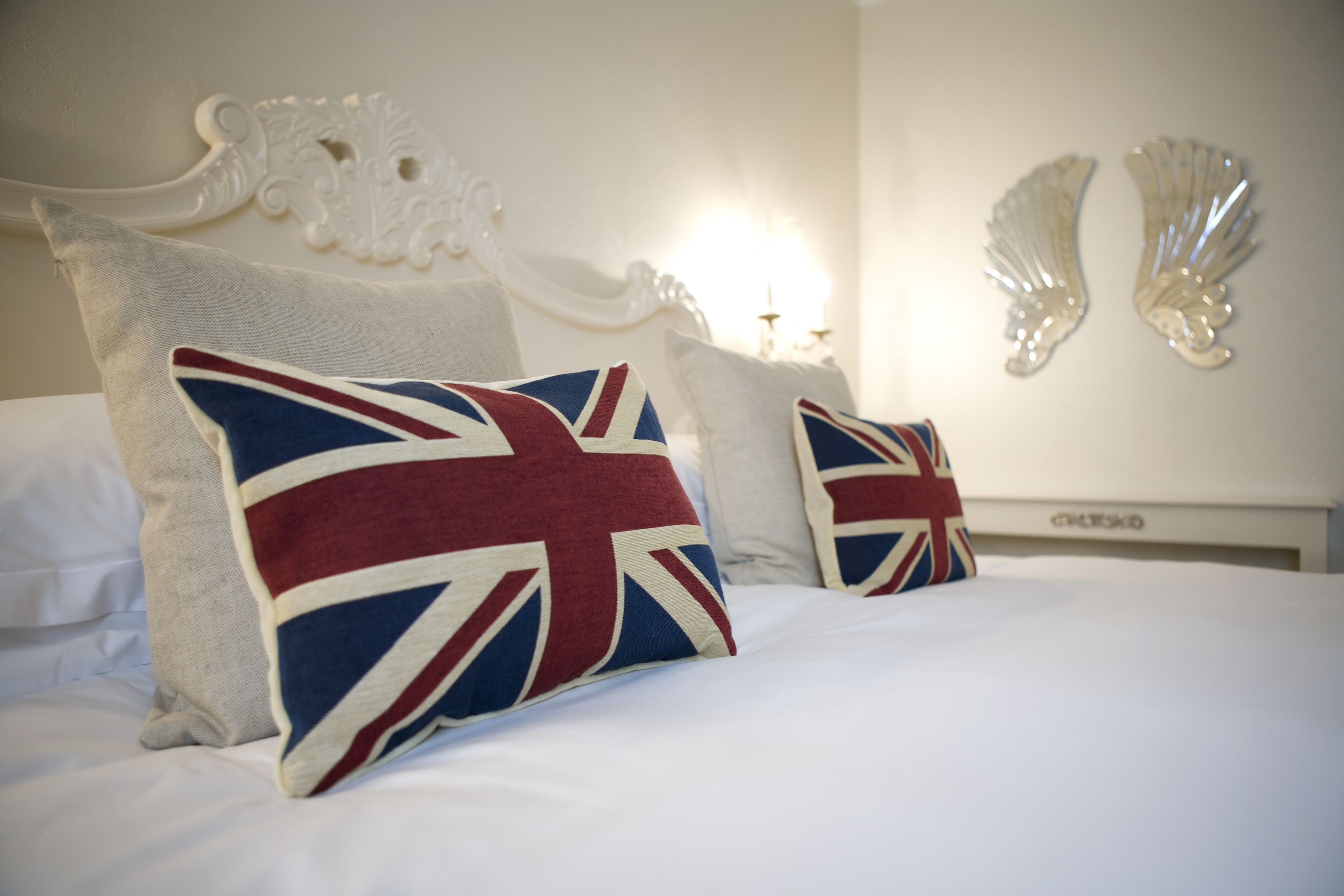 Ein ordentlich bezogenes Bett mit Kissen im Union-Jack-Design, ein weißes verziertes Kopfteil und ein an der Wand befestigtes dekoratives Element.
