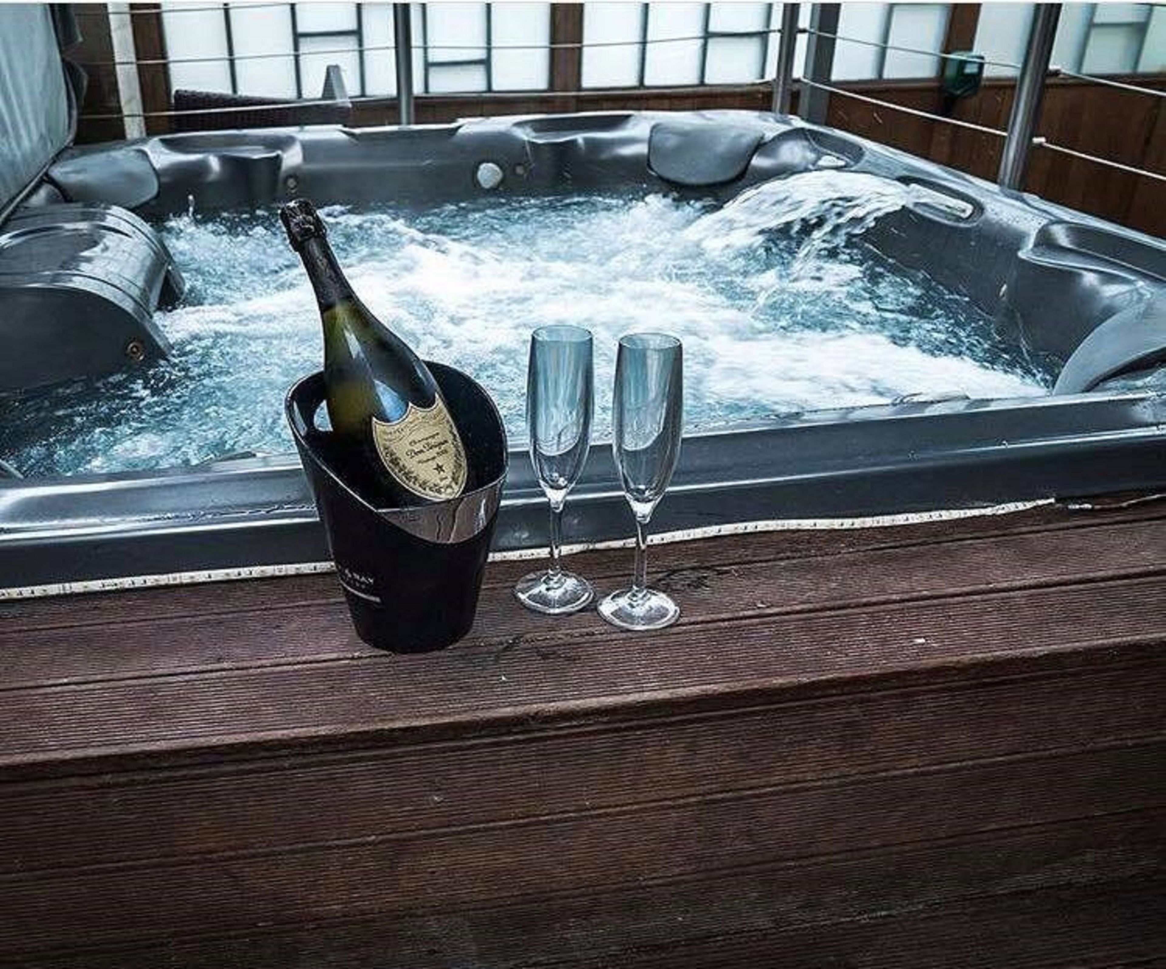 A hot tub with a bottle of champagne and two glasses on a wooden deck.
