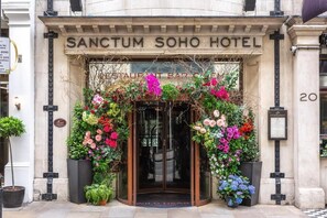 The entrance of Sanctum Soho Hotel with a glass door, surrounded by floral decorations and a sign indicating a restaurant bar cafe. - Karma Sanctum Soho (London)