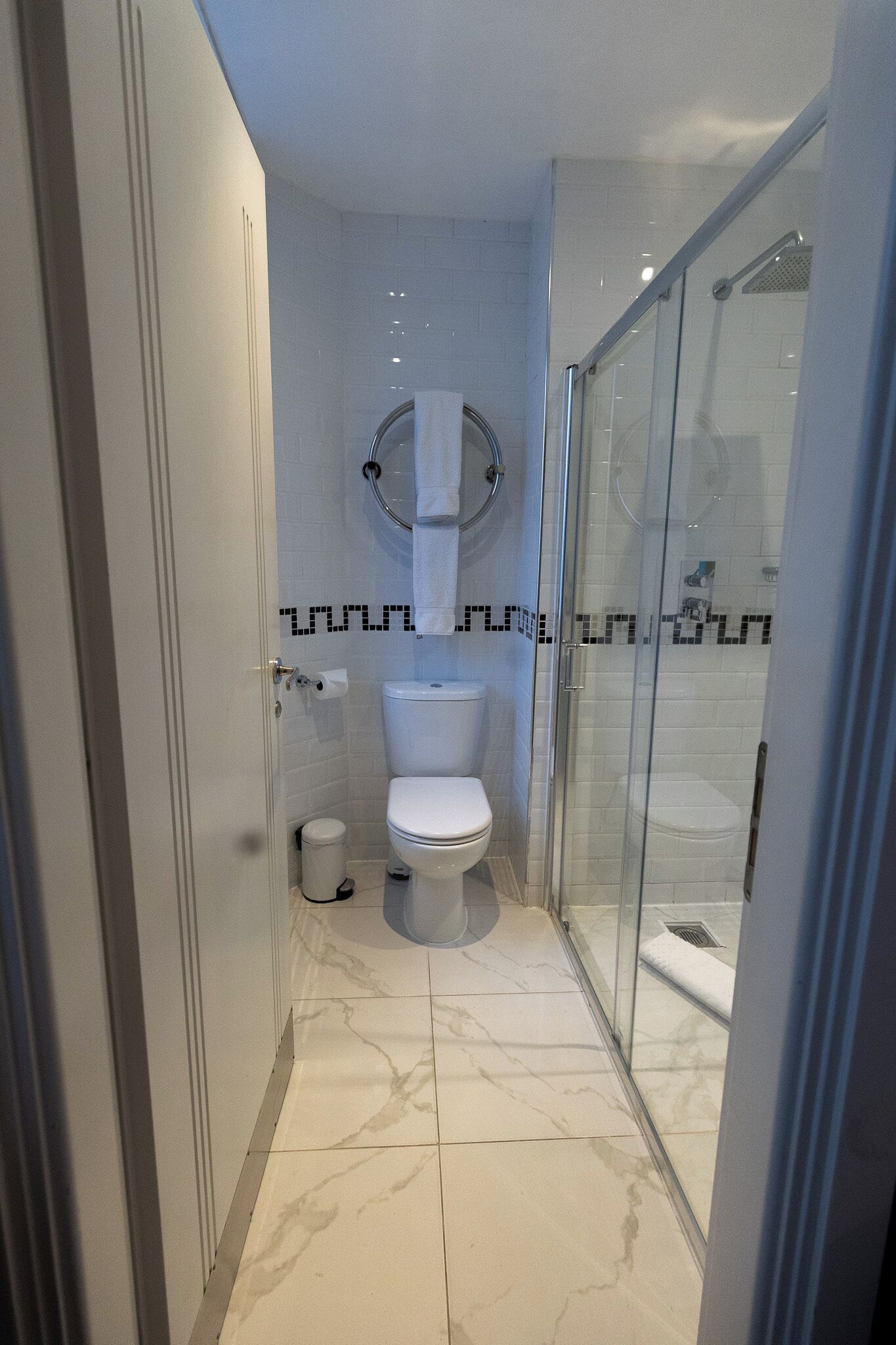 A modern bathroom with a glass-enclosed shower, a toilet, and a marble-tiled floor.