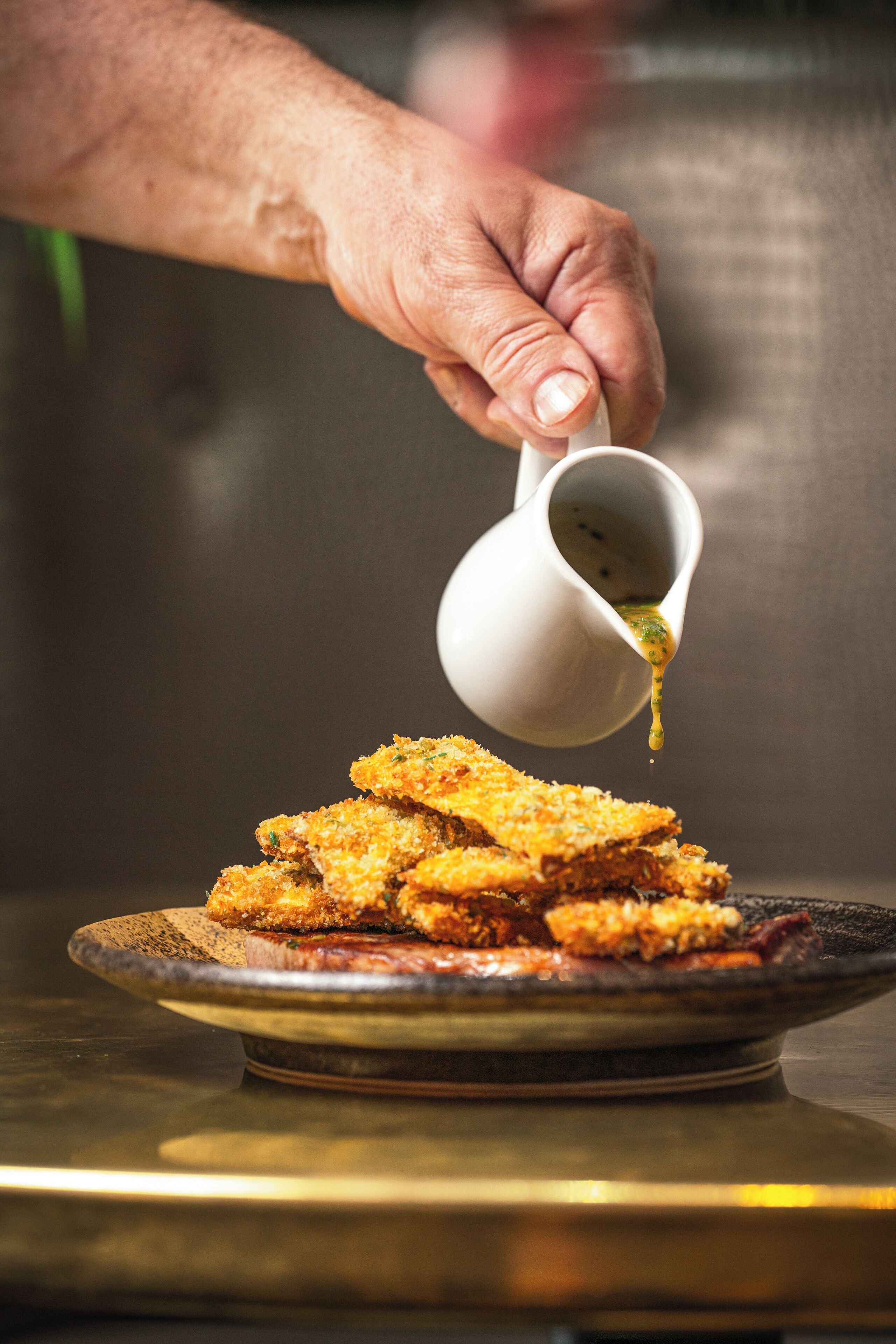 A hand pouring sauce over a plate of breaded food.