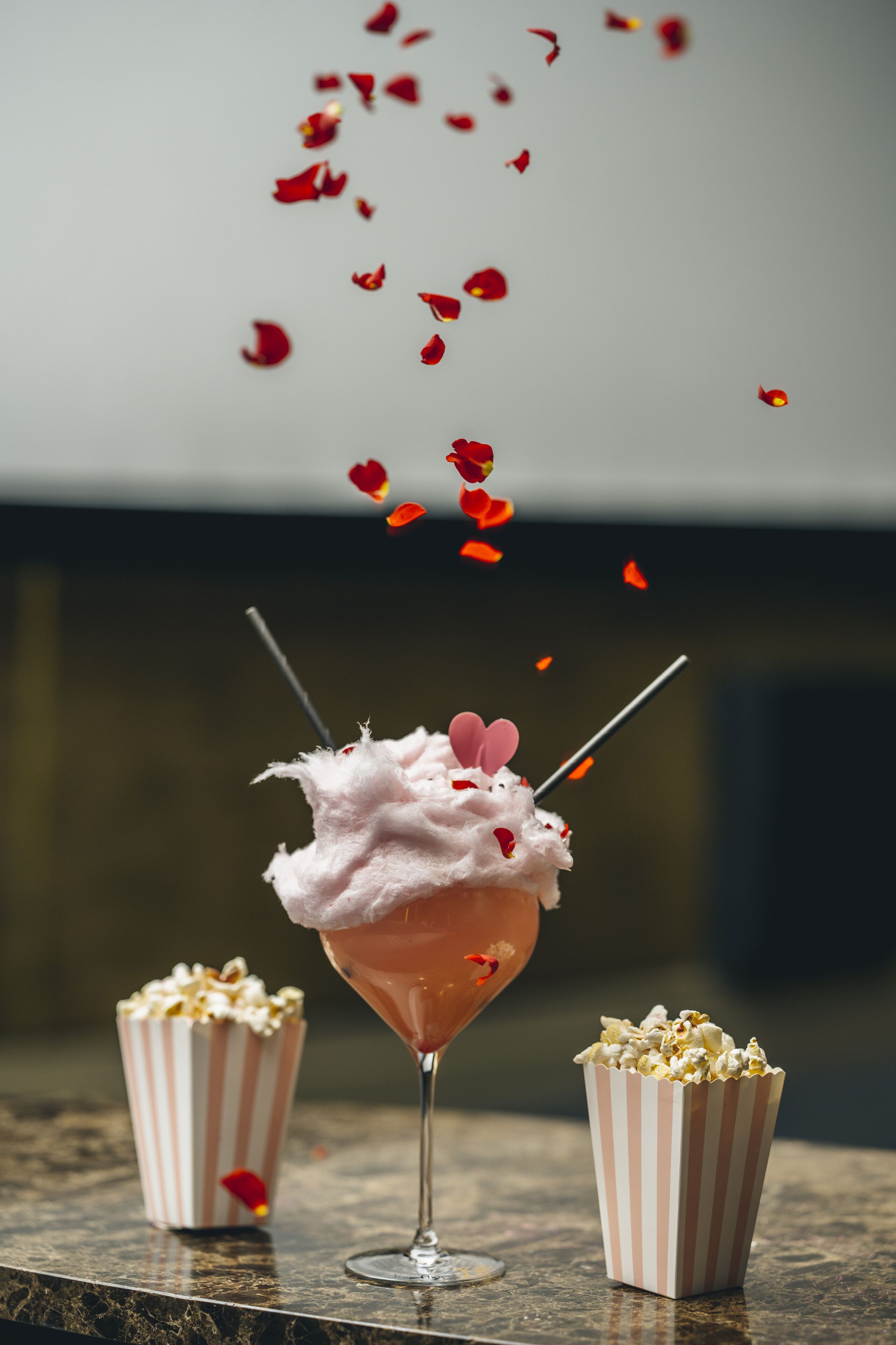 A martini glass with a pink drink, a striped popcorn container, and a second empty container.