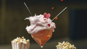 A martini glass with a pink drink, a striped popcorn container, and a second empty container.