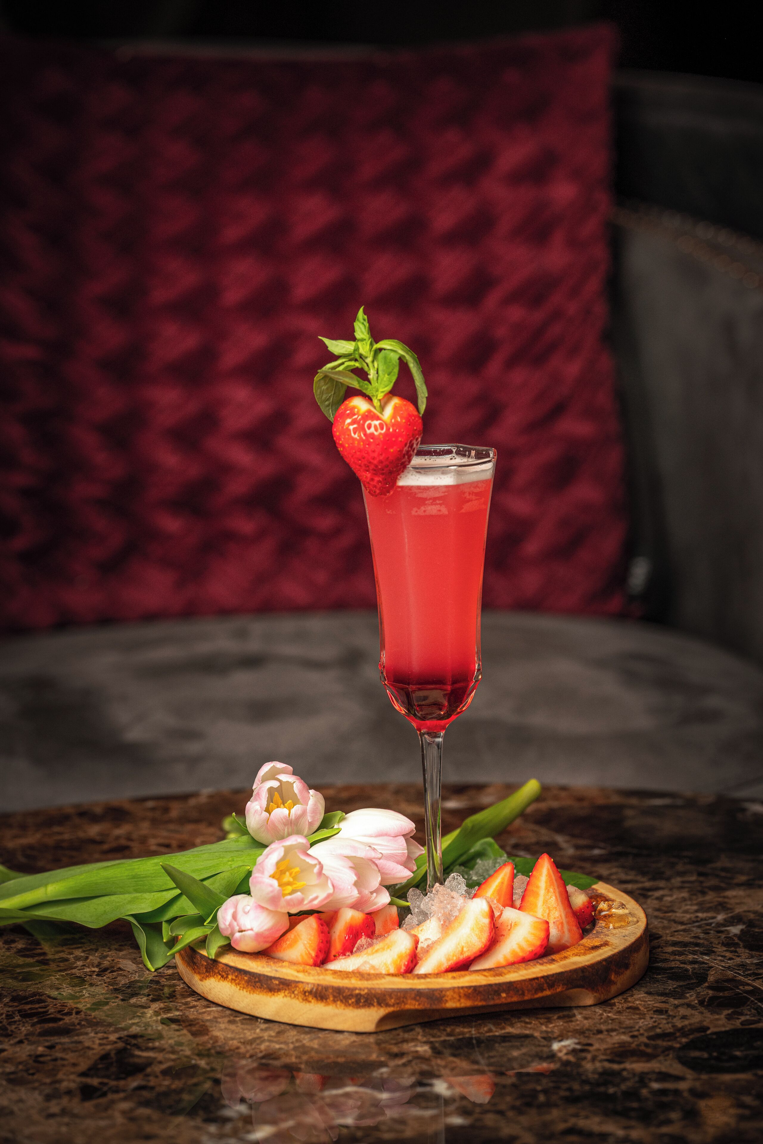 Prato com morangos e um copo de bebida vermelha, possivelmente um cocktail, sobre uma mesa de mármore.