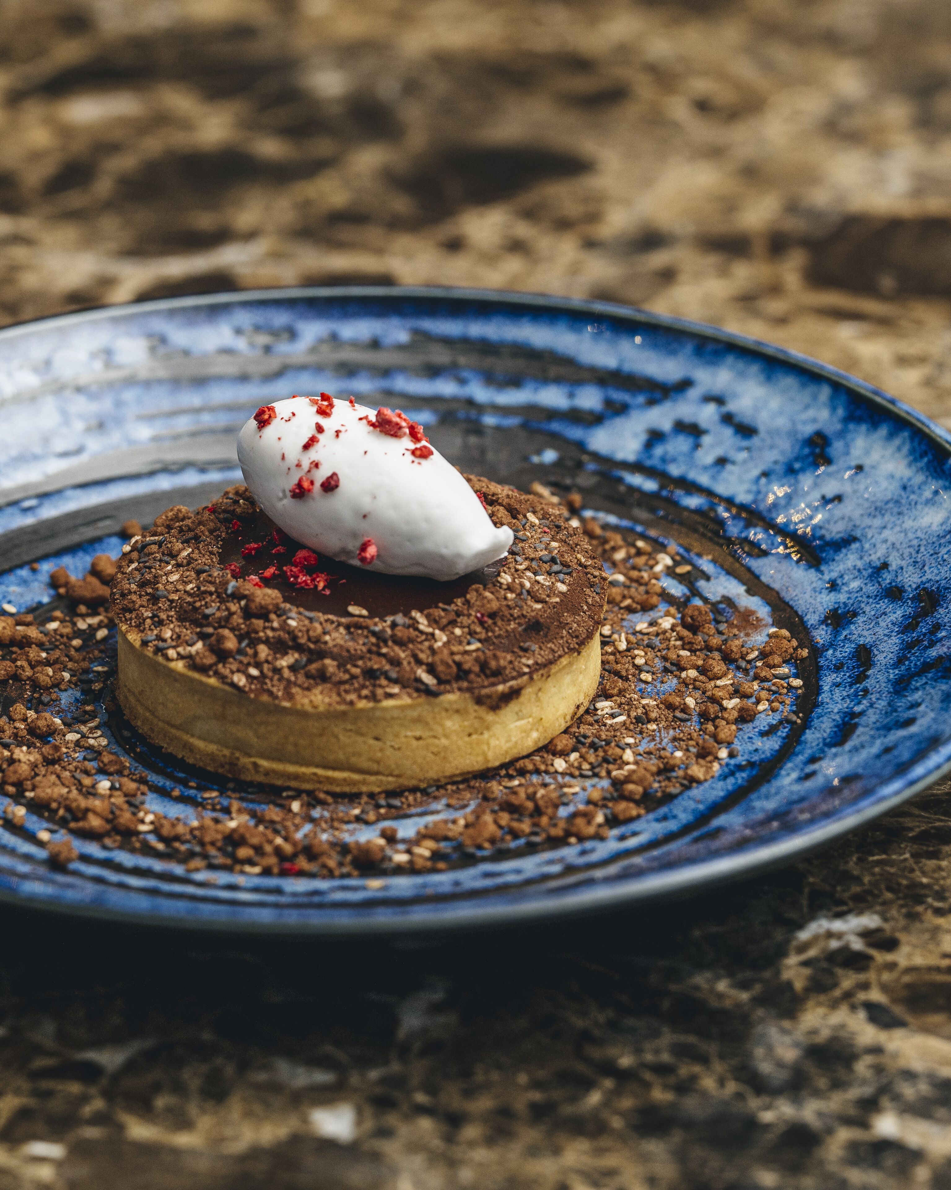 A dessert on a blue plate with a crumbly topping and a dollop of cream on top.