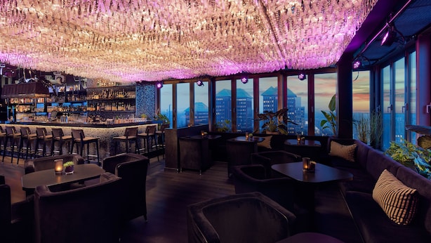 Un área de bar con vistas a la ciudad, distribución de asientos y un techo decorativo.