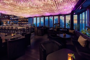 Un área de bar con vistas a la ciudad, distribución de asientos y un techo decorativo.