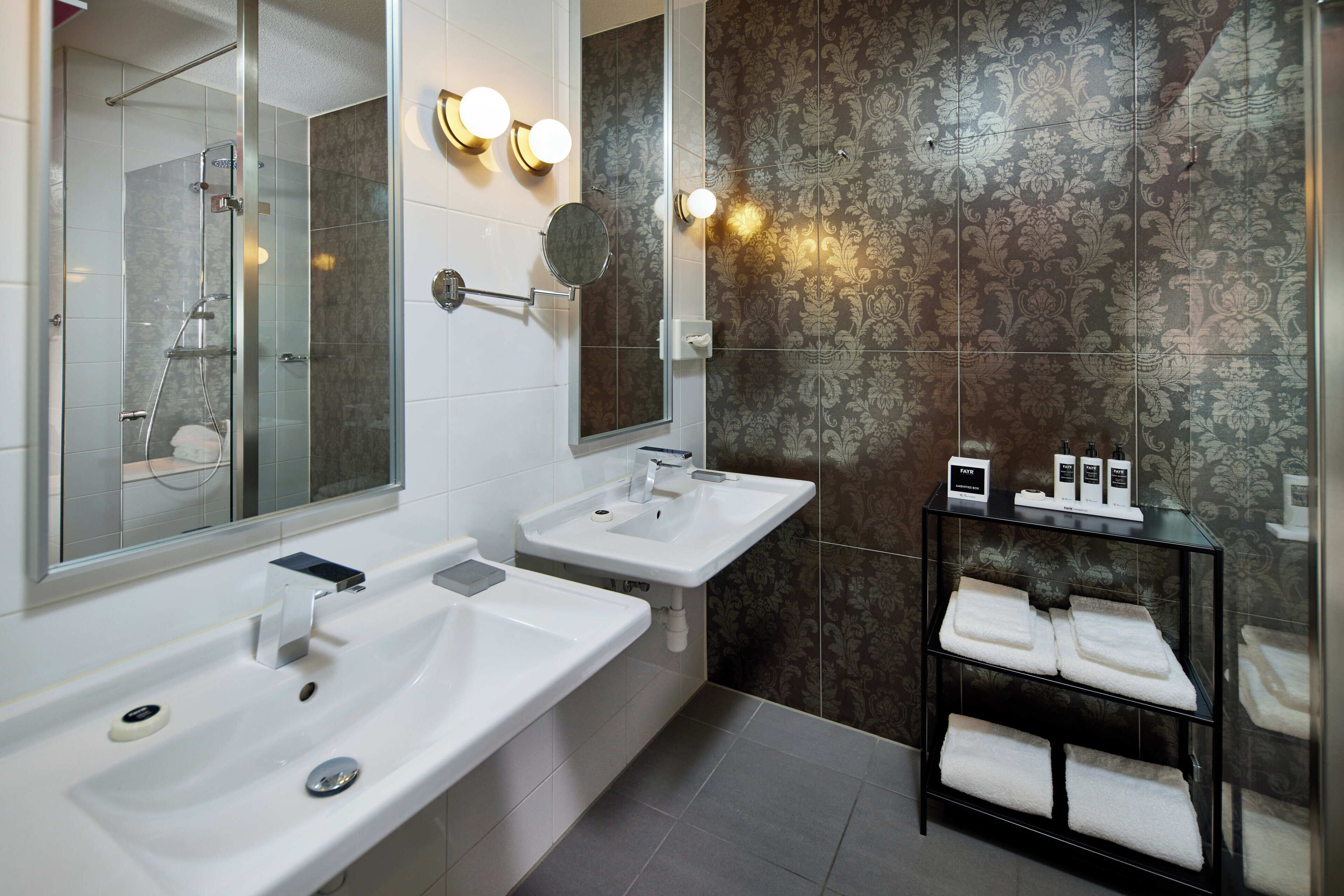 A modern bathroom with two sinks, a glass shower enclosure, and a towel rack with neatly folded towels.