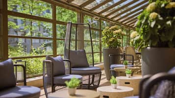 A sunlit indoor seating area with wicker furniture and potted plants.
