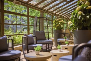 Et solbeskinnet opholdsområde indendørs med fletningsmøbler og potteplanter.