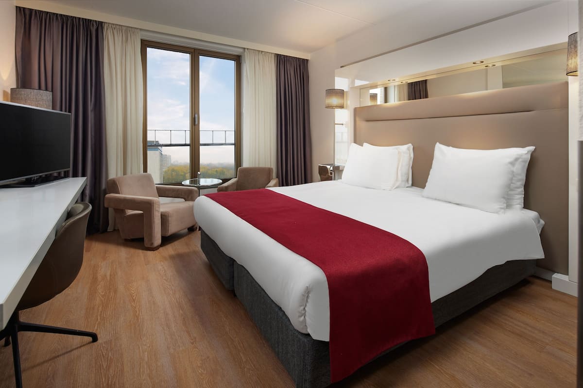 Een hotelkamer met een bed, een bureau, een stoel, een televisie en een balkon met gordijnen.