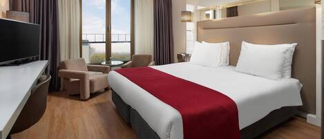 A hotel room with a bed, a desk, a chair, a TV, and a balcony with curtains.