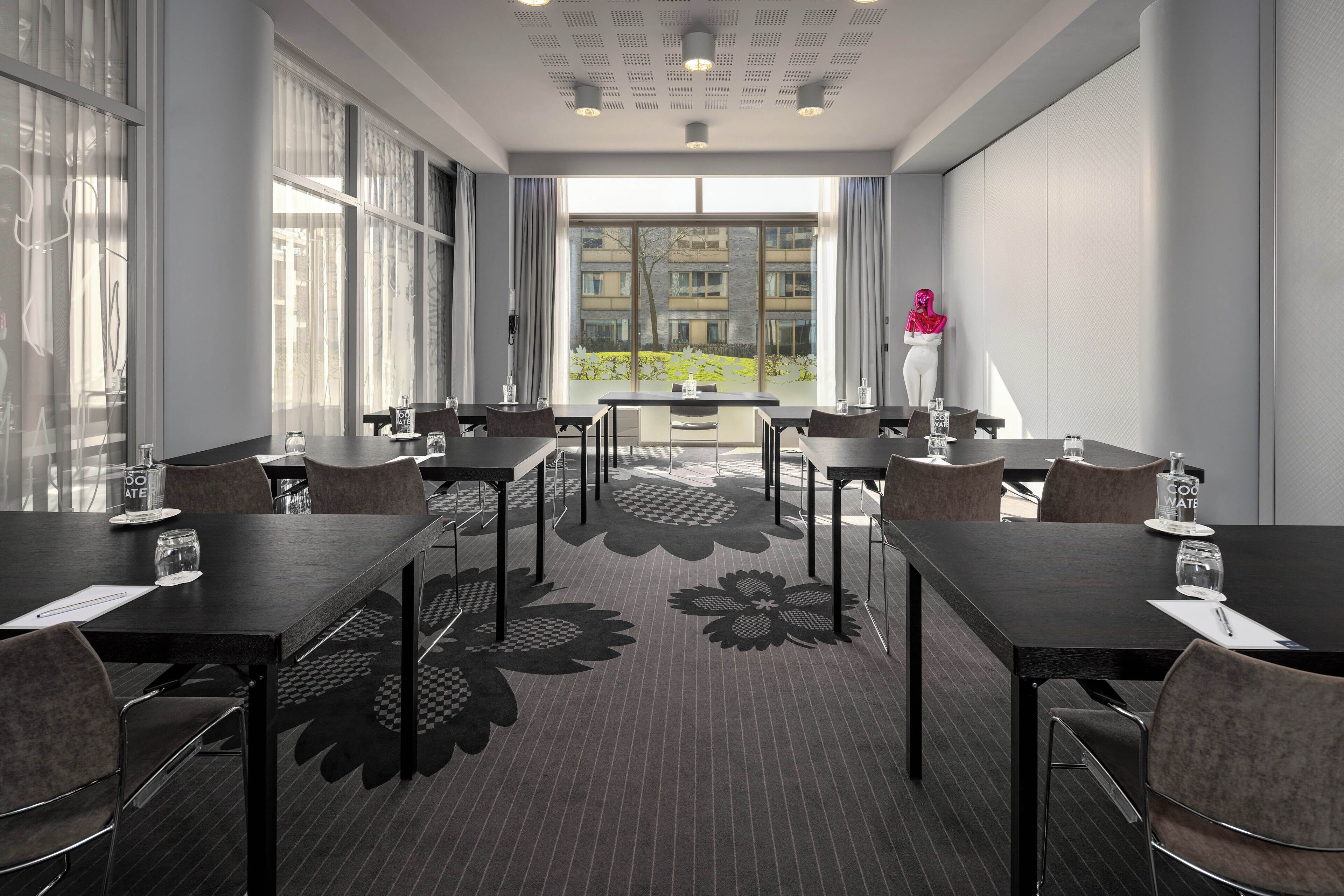 A conference room with tables and chairs, large windows, and a view of buildings outside.