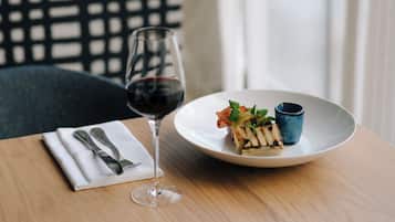 A dining table with a white plate containing a grilled dish, a small blue cup, and a glass of red wine.