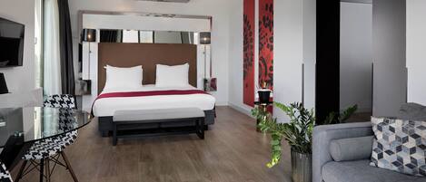 A modern hotel room with a large bed, a seating area with a sofa and chairs, a flat-screen TV, and a ceiling with a floral design.