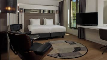 Une chambre d’hôtel avec un lit, un bureau, une chaise, une télévision et une fenêtre avec des rideaux.