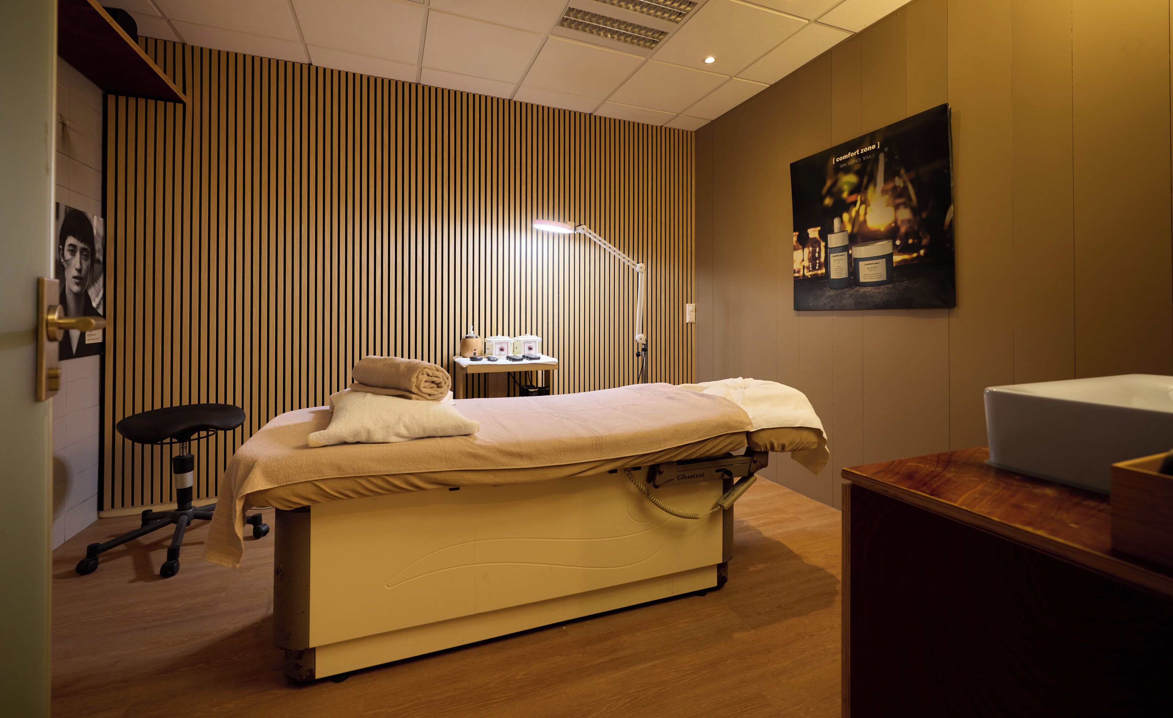 A room with a bed, a desk, a chair, a lamp, and a poster on the wall.