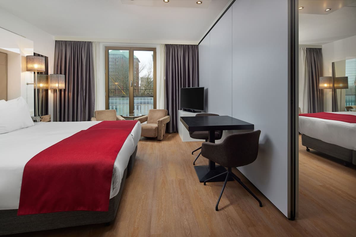 Een moderne hotelkamer met een groot bed, een bureau, een stoel, een televisie en uitzicht op een balkon.