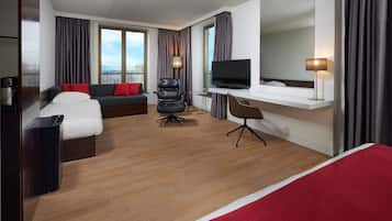Habitació d'hotel amb llit, sofà, escriptori, cadira, televisió i finestra gran.