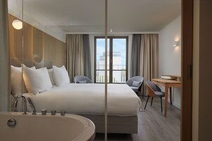 Une chambre d’hôtel moderne dotée d’un grand lit, d’un bureau, d’une chaise, d’une baignoire et offrant une vue sur la ville par la fenêtre.