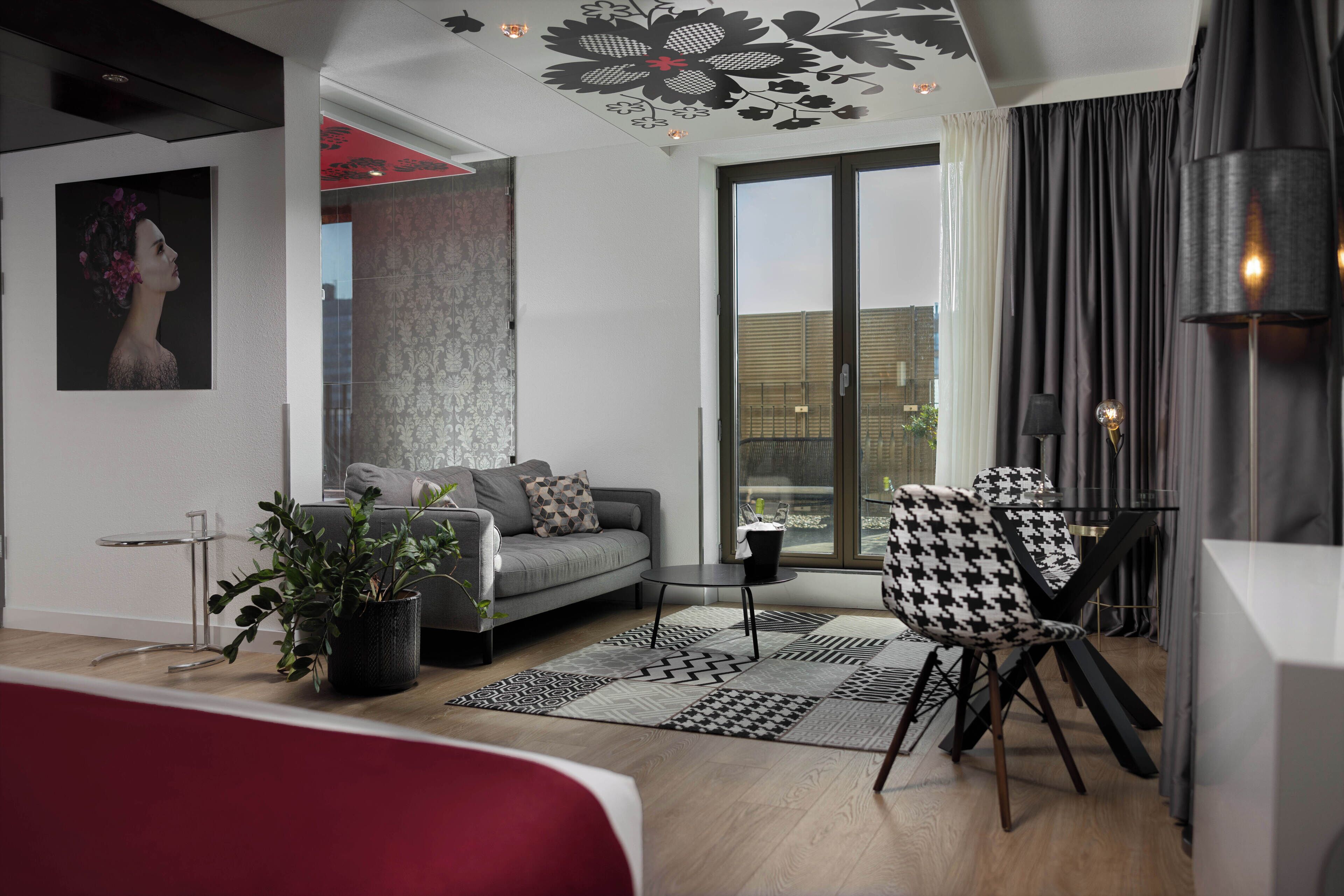 A modern living room with a grey sofa, black and white houndstooth chair, a small round table, and a potted plant.