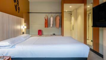 Habitación de hotel con una cama grande, una mesita de noche, un espejo y un televisor montado en la pared.