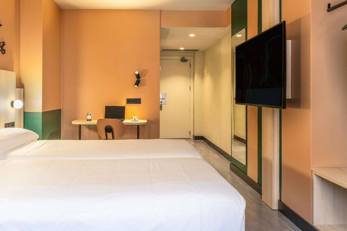 A hotel room with a bed, a desk with a chair, a television, and a door leading to another room.