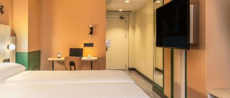 Una habitación de hotel con una cama, un escritorio con una silla, un televisor y una puerta que da a otra habitación.