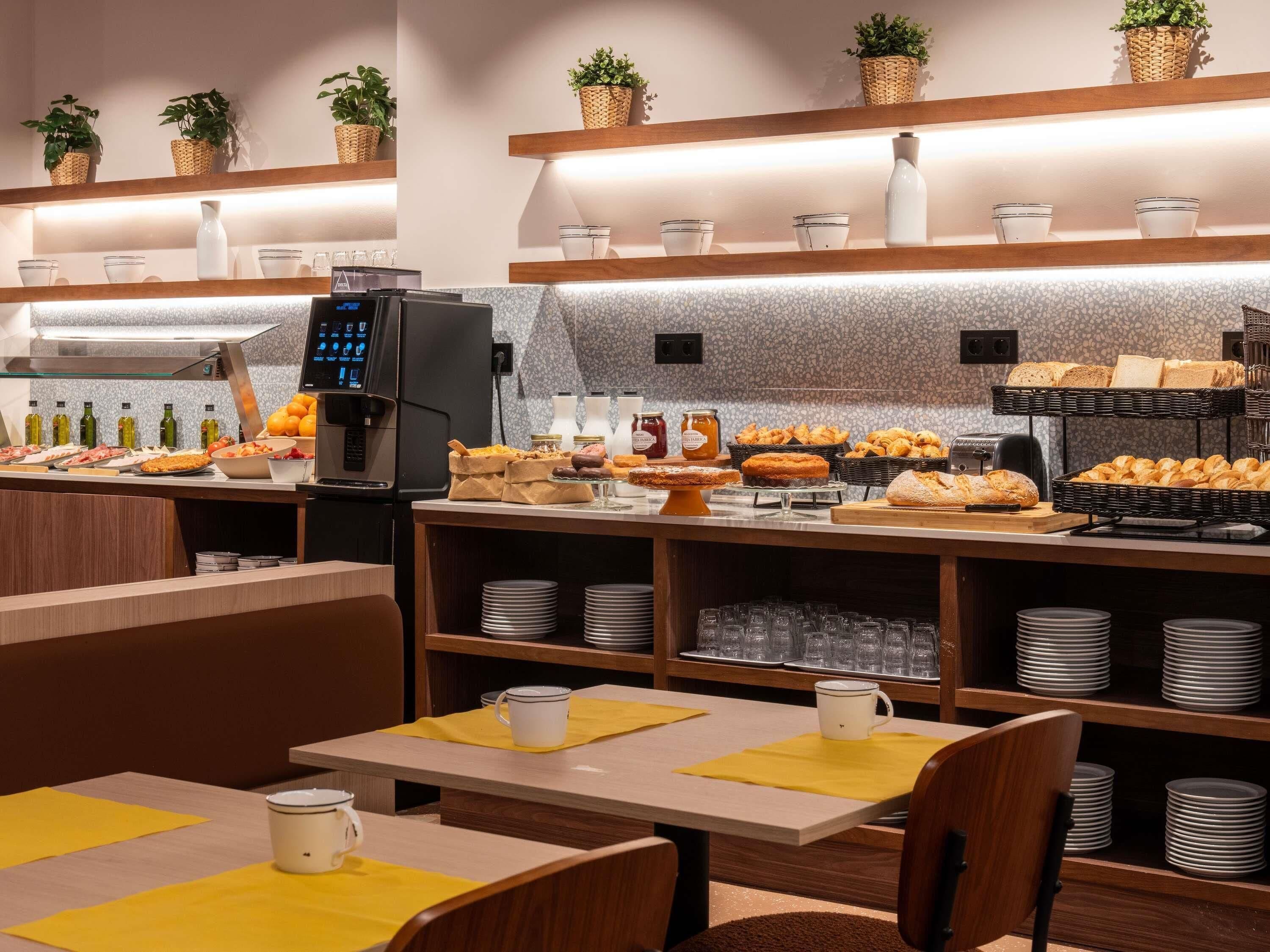 A breakfast buffet with various food items, a coffee machine, and neatly arranged plates and cups.