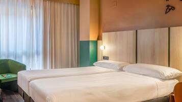 A hotel room with two beds, a green chair, and a wall-mounted light fixture.