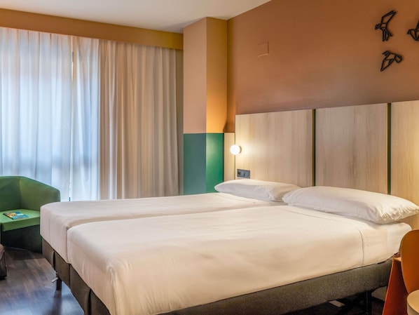 Una habitación de hotel con dos camas, una silla verde y una lámpara fijada a la pared.