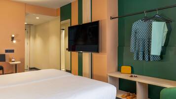 Habitación de hotel con cama, televisión, espejo, escritorio y silla.