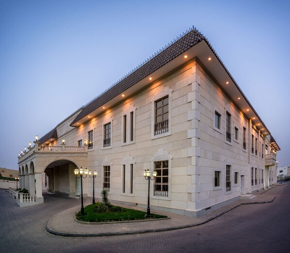Een groot, lichtkleurig gebouw met een pannendak, meerdere ramen en een overdekte ingang.