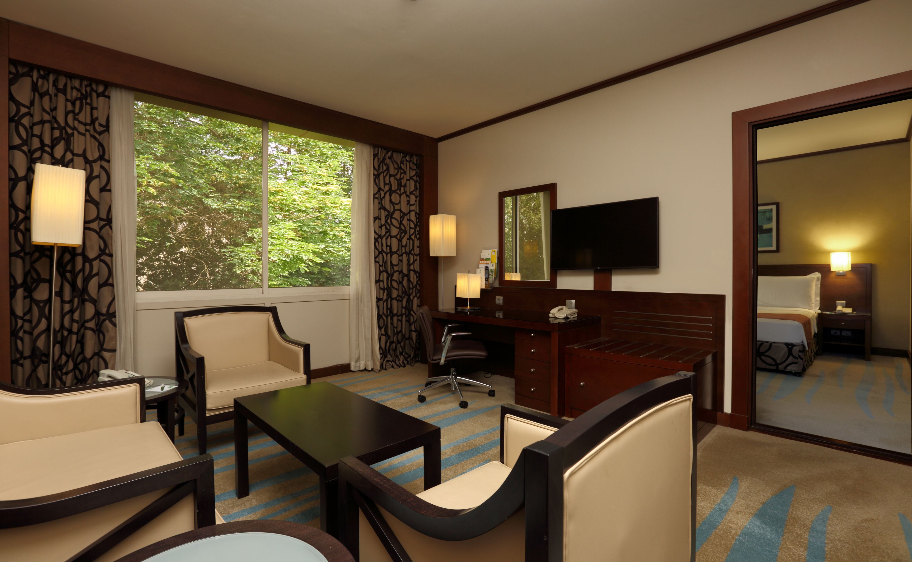 Ein Hotelzimmer mit großem Fenster, Schreibtisch, Stuhl, Bett und Fernseher.