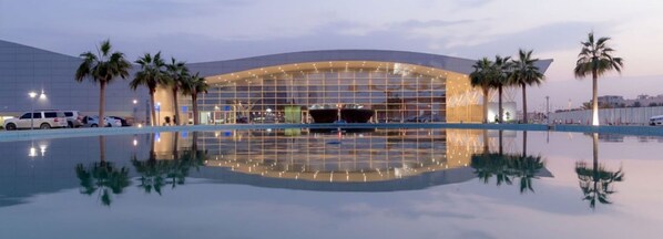 A modern hotel with a large glass facade, palm trees, and a pool reflecting the building. - Holiday Inn Riyadh Izdihar by IHG (Riyadh)